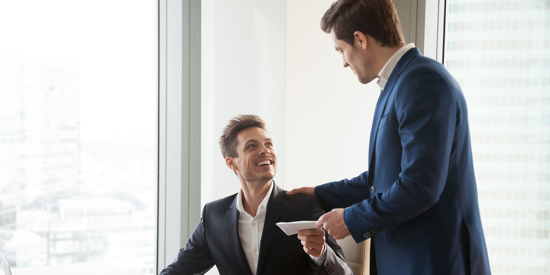 Unternehmer überreicht seinem Mitarbeiter seinen Lohn oder seinen Bonus in einem Umschlag.