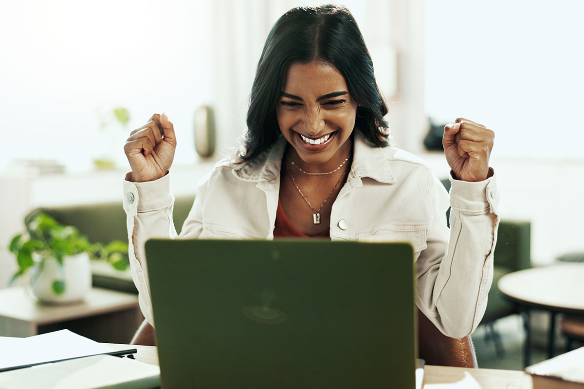Mitarbeiterin sitzt sich am Laptop und freut sich über die Nachricht, dass sie aufgrund ihrer Leistung einen Bonus erhält.