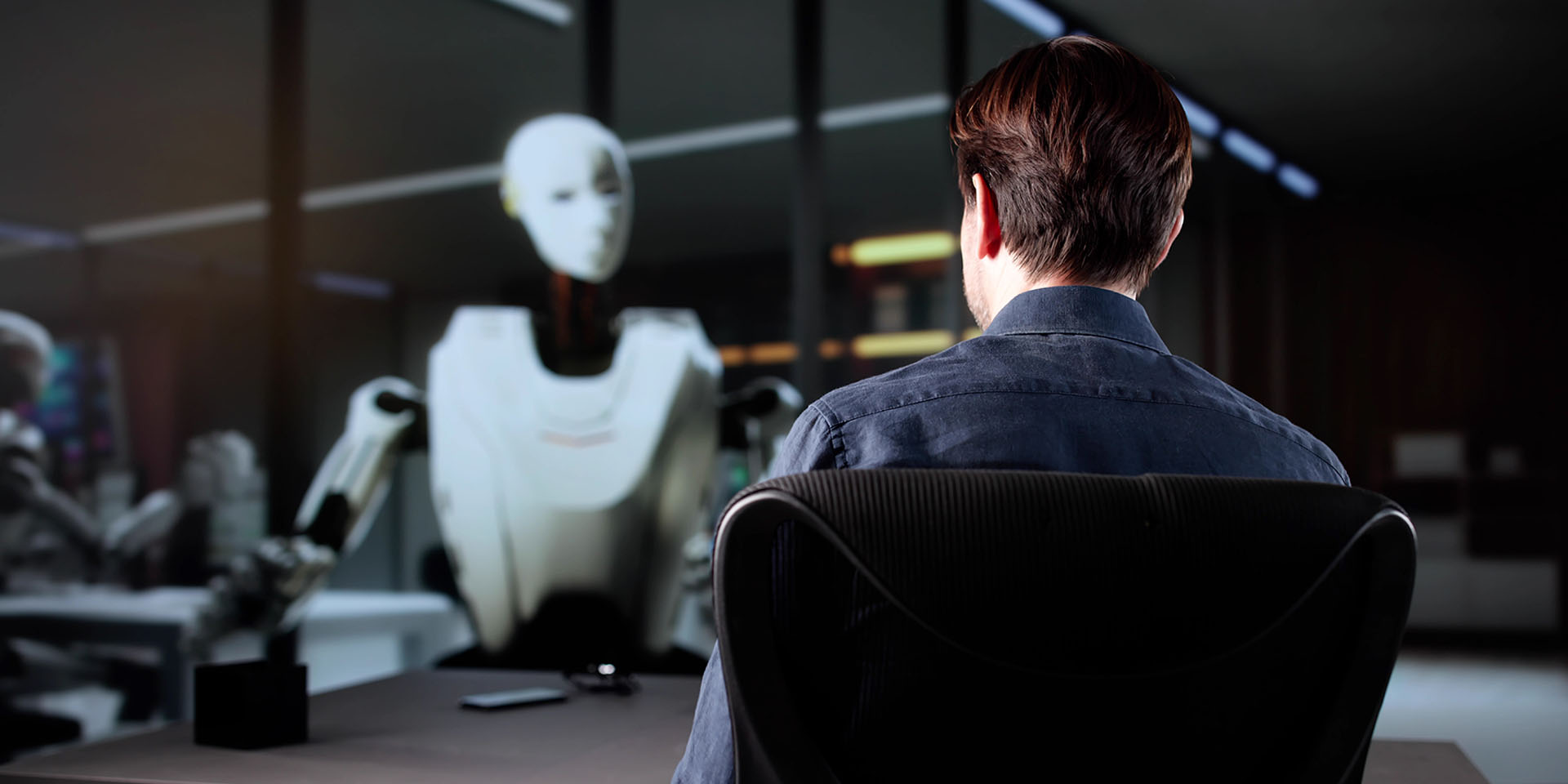 Mann sitzt an einem Schreibtisch und spricht in einem modernen Büro mit einem humanoiden KI-Roboter.